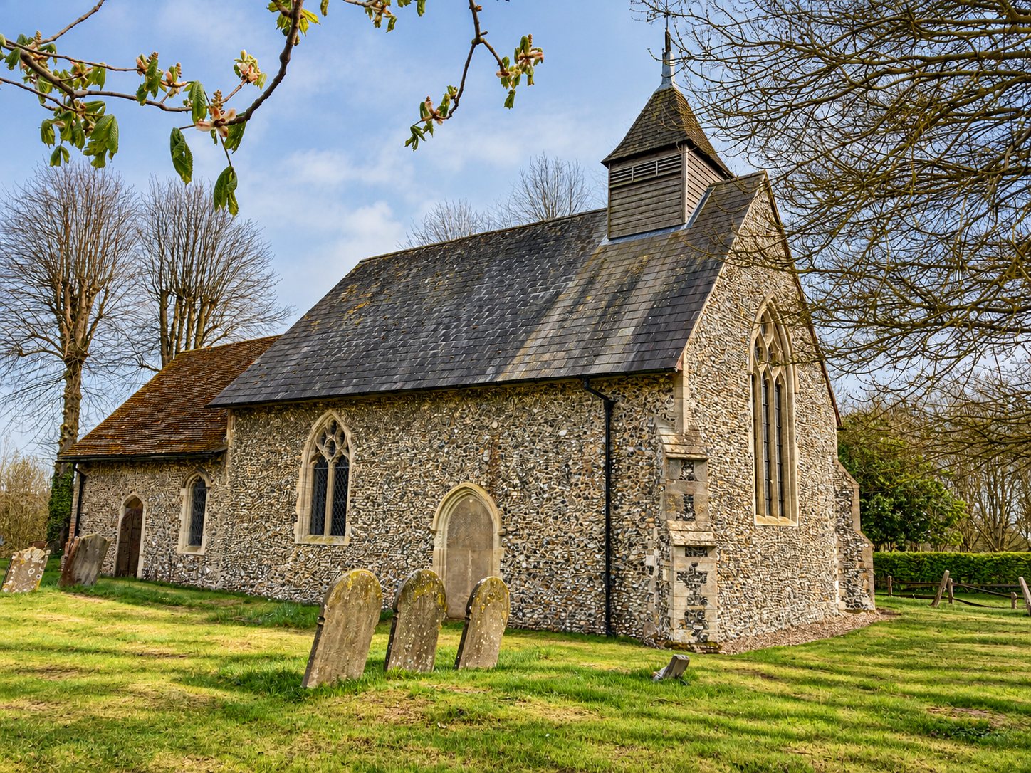 Flint parish church with a timber bell turret and slate roof, seen across the churchyard