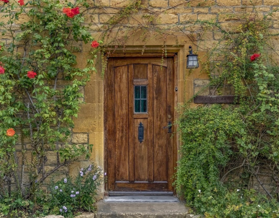 Oak front door in a honey stone cottage wall, framed by climbing roses