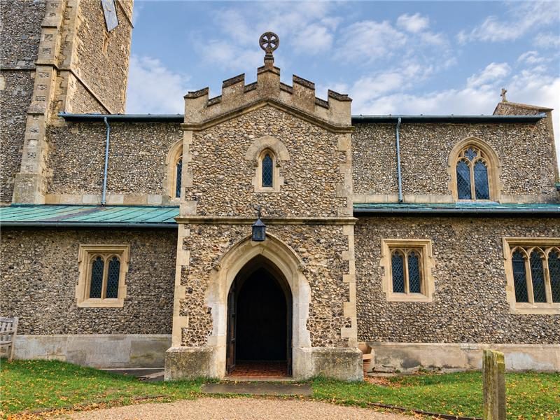 Flint church with a crenellated stone porch and an arched oak door