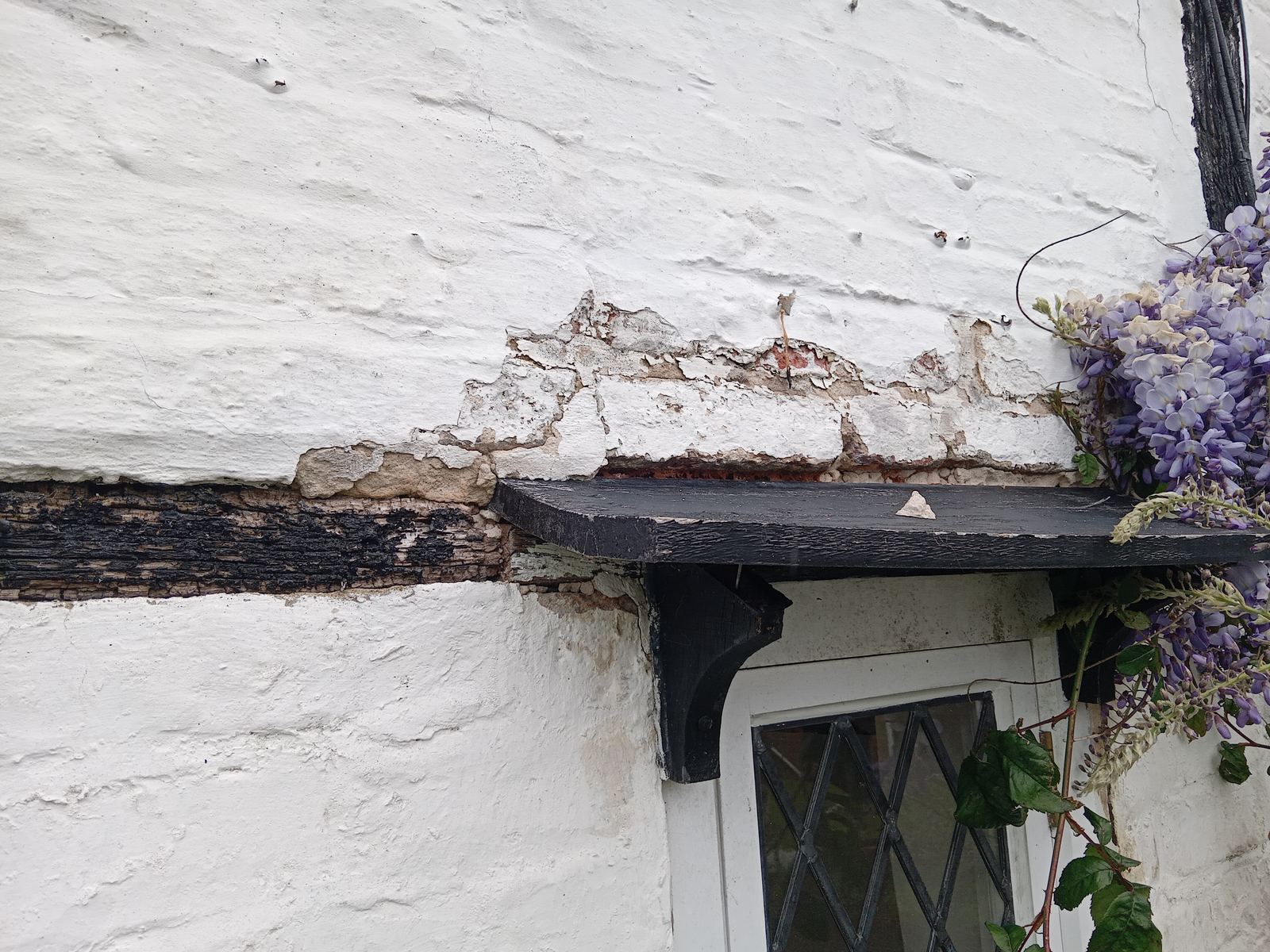 Decayed render and timber beam above a cottage doorway, photo 1 of 2