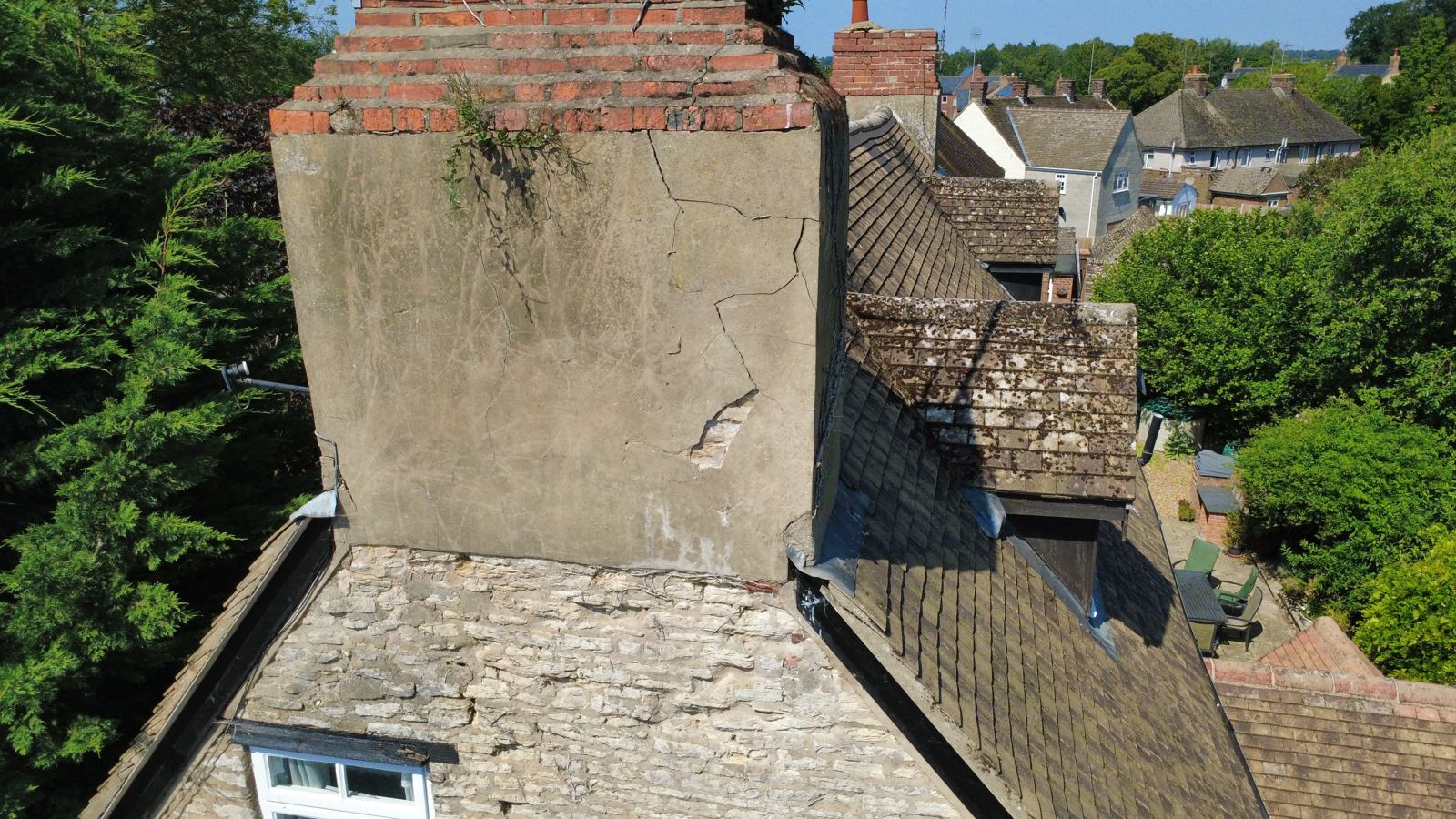 Drone view of a cracked rendered chimney stack with plants rooting in the brick capping, photo 2 of 4