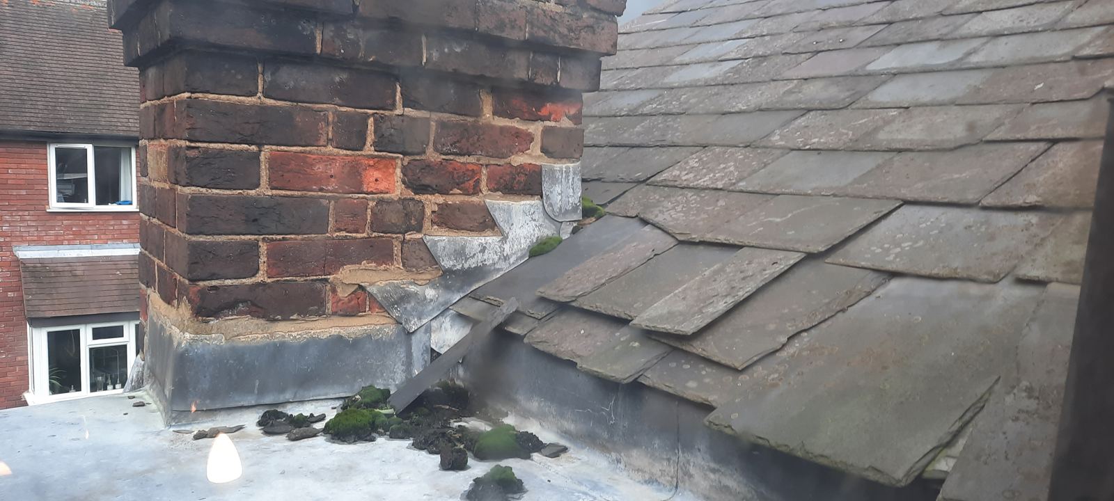 Chimney stack with eroded mortar, patched lead flashings and moss on a flat roof, photo 3 of 4