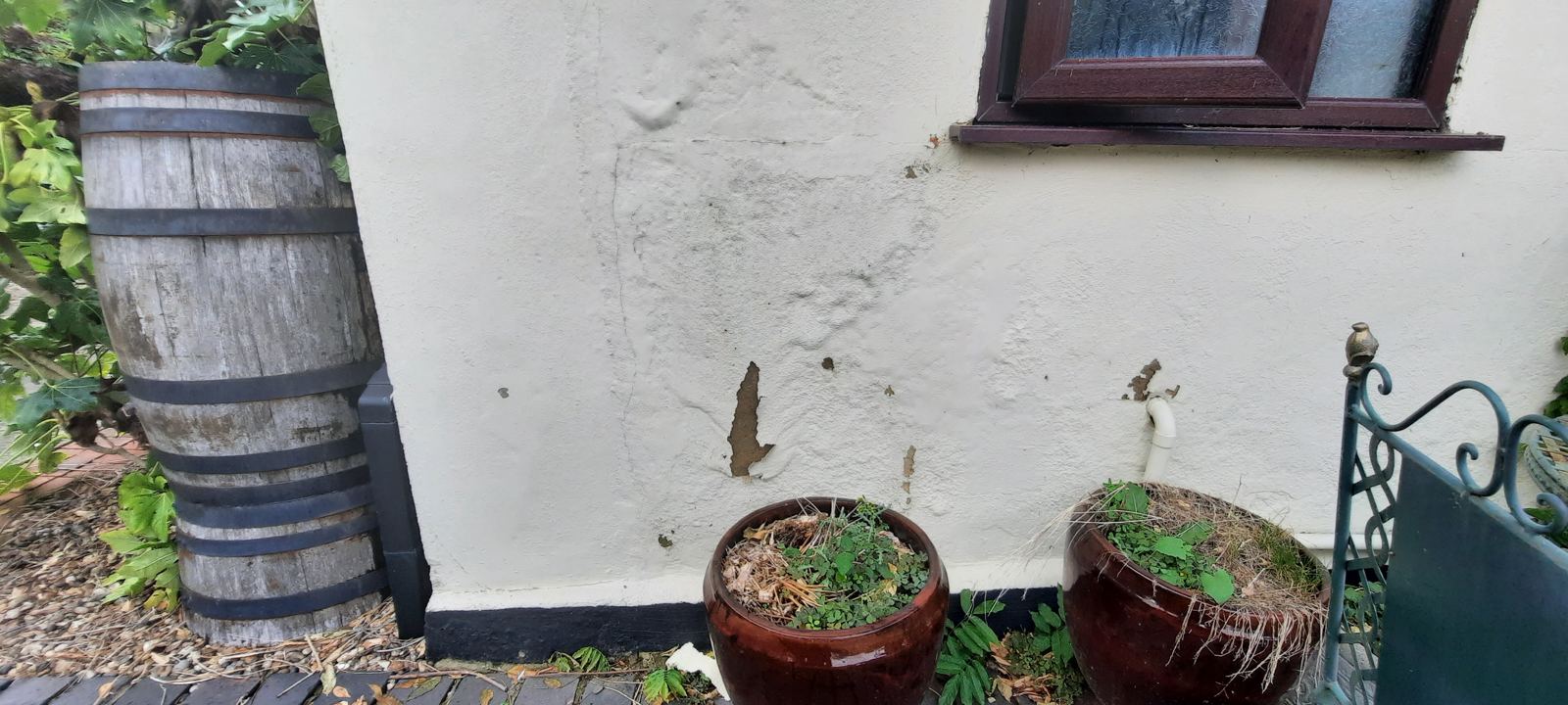 Rendered wall with bulging and flaking patches above a black plinth, photo 4 of 4