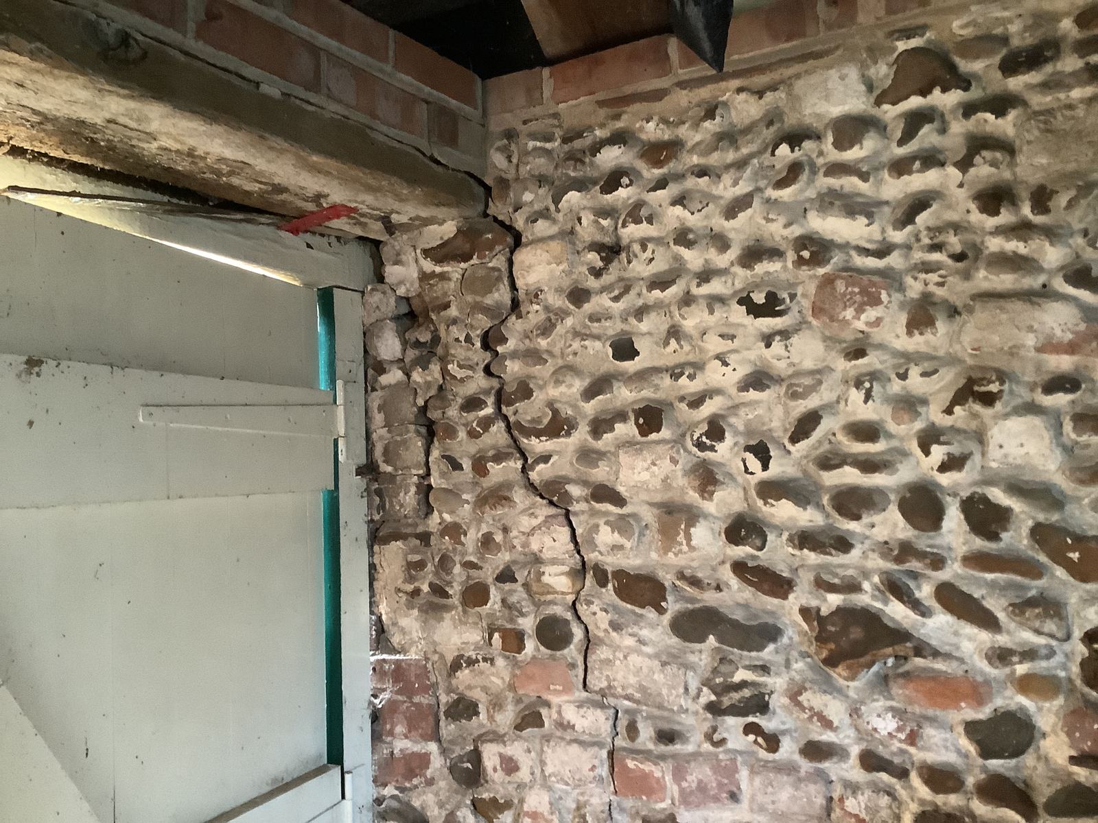 Vertical crack running through flint and brick walling beside a timber door, photo 1 of 4