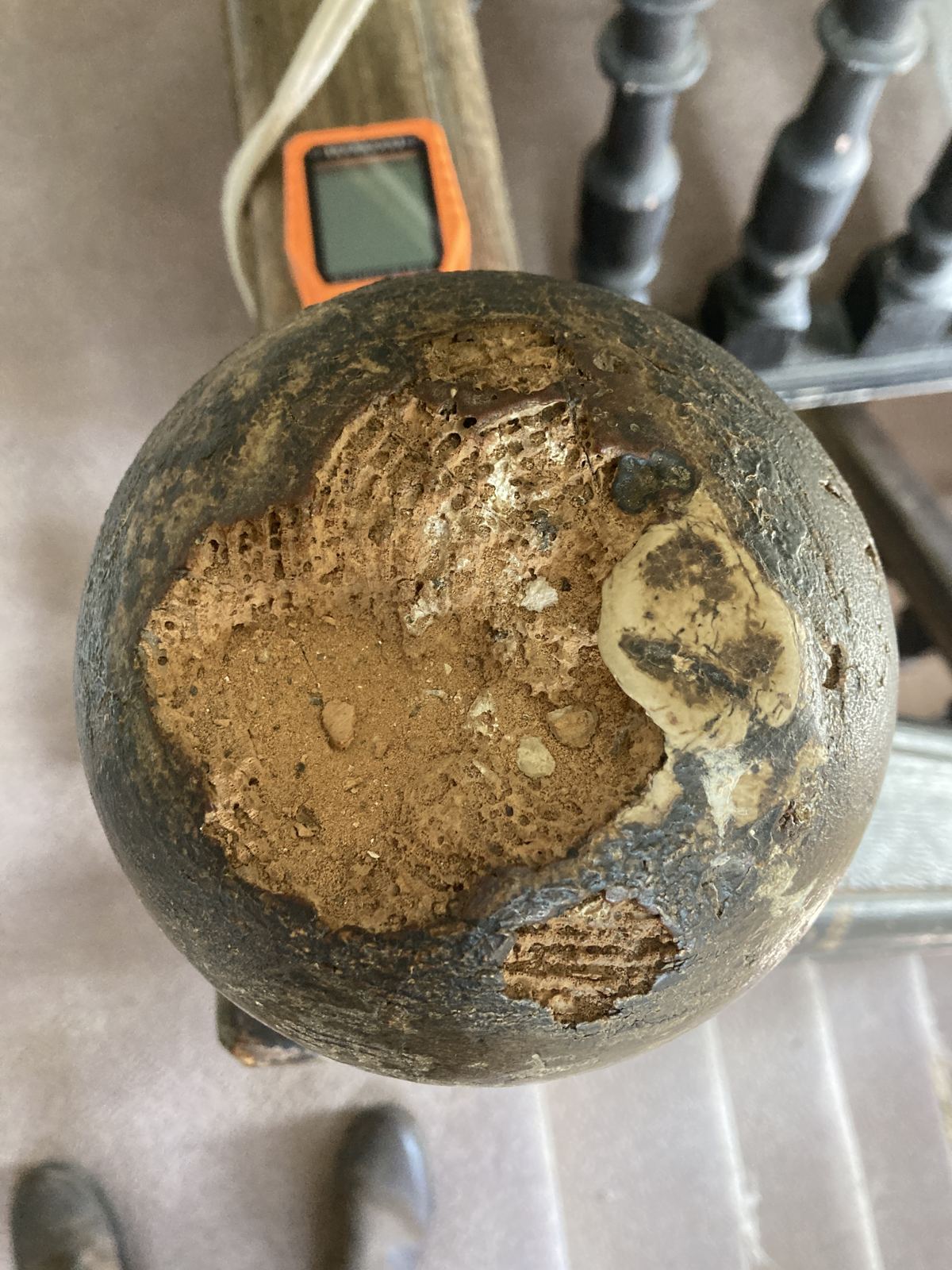 Newel post cap hollowed out by wet rot, beside a moisture meter, photo 2 of 4