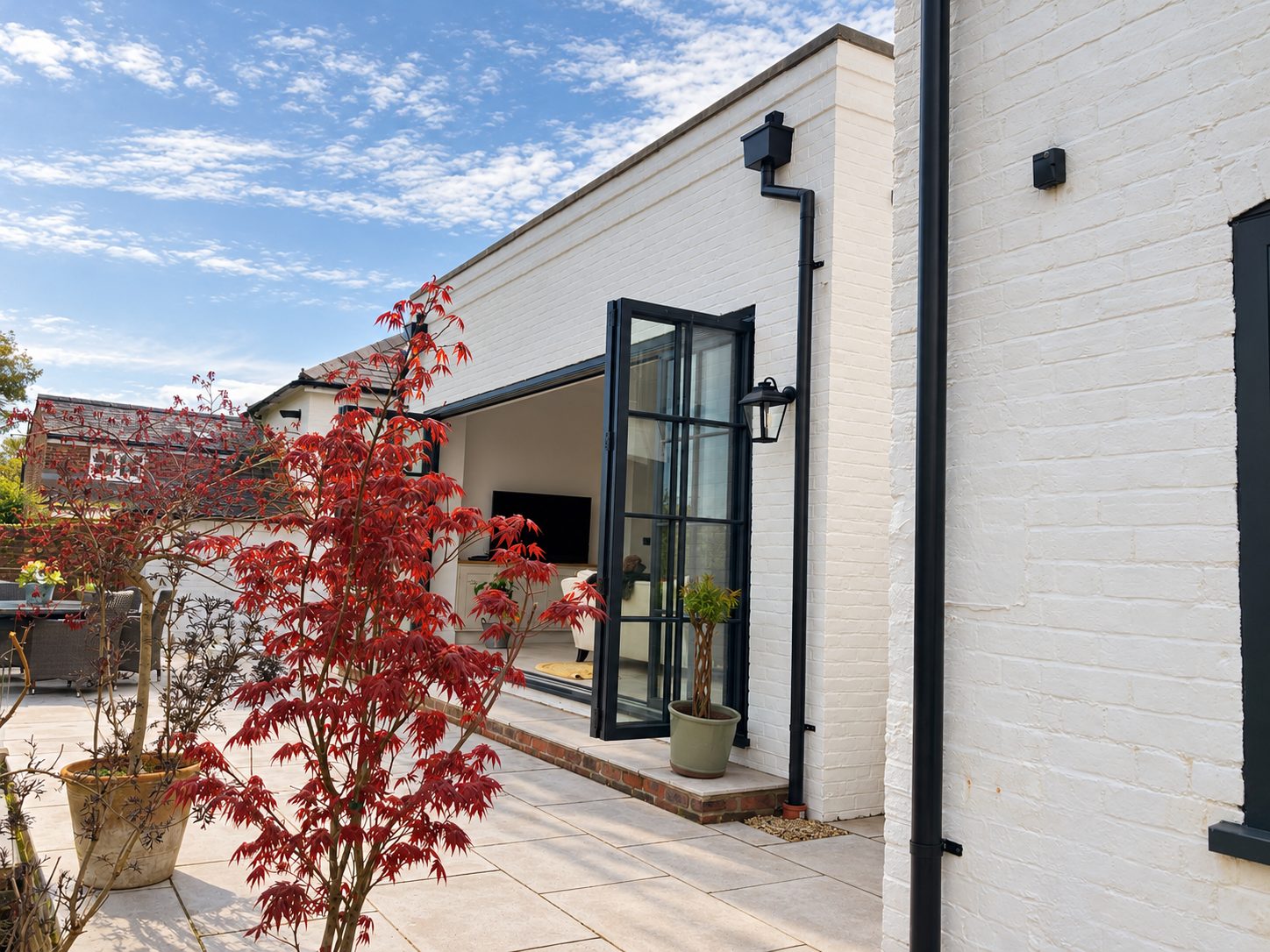 Painted brick garden room with open crittall-style doors and a red acer