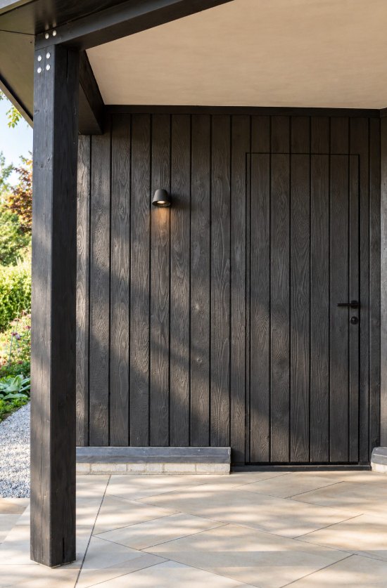 Charred timber cladding with a flush hidden door under an oak-framed porch