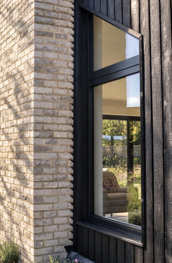 Pale brick corner beside a deep-set window in charred timber cladding